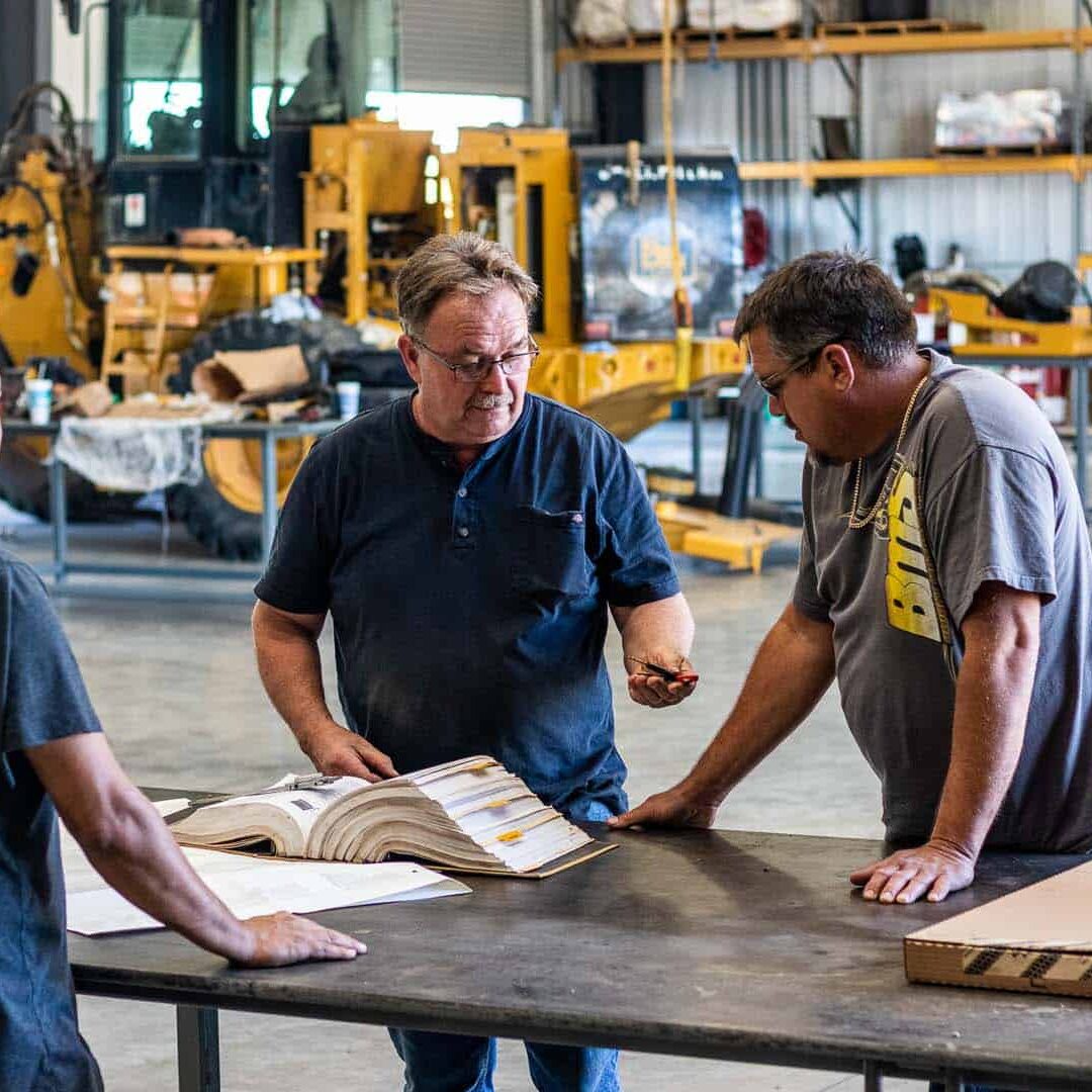 Three men looking at a small piece of equipment